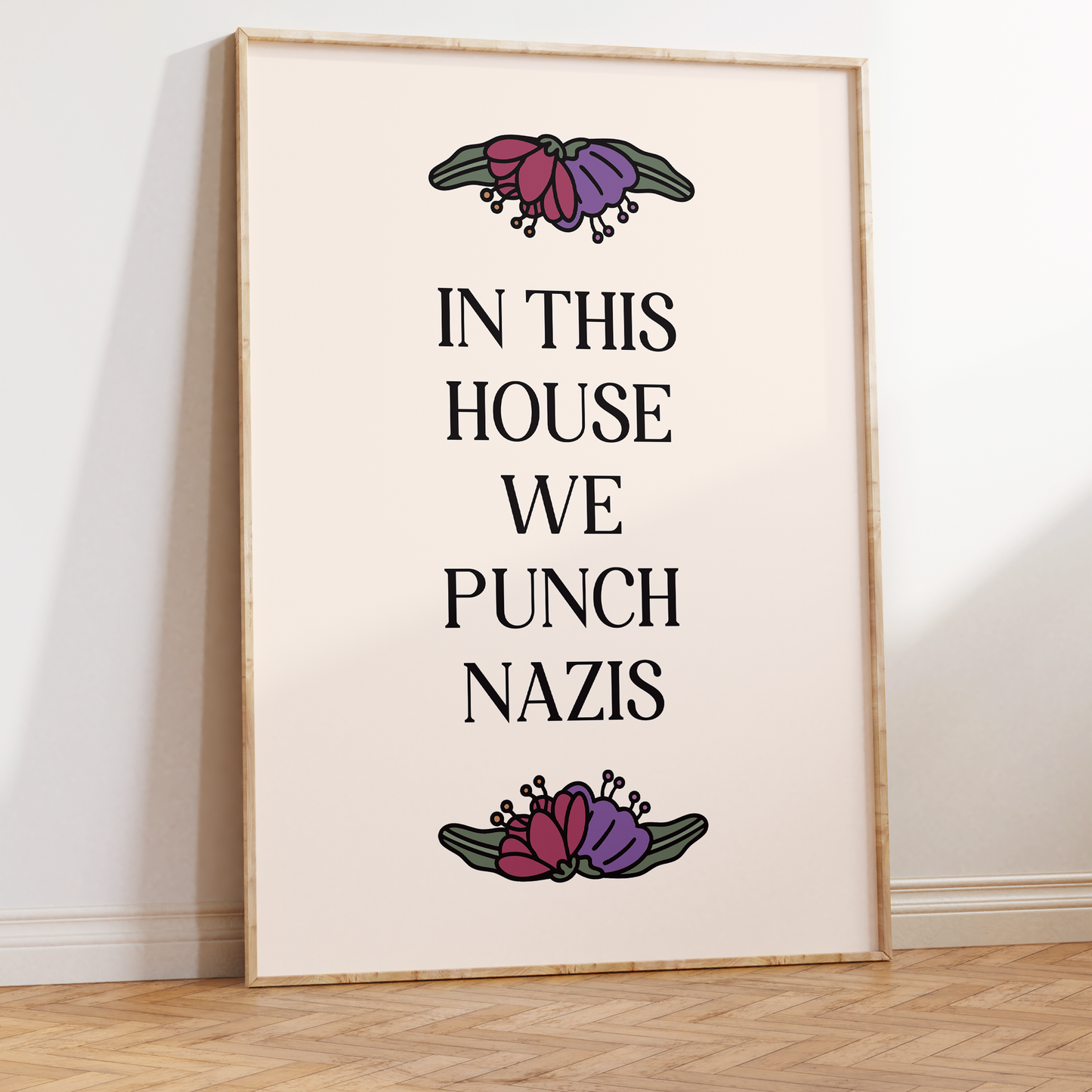 Framed poster with text 'In this house we punch nazis' and floral designs on a white wall.