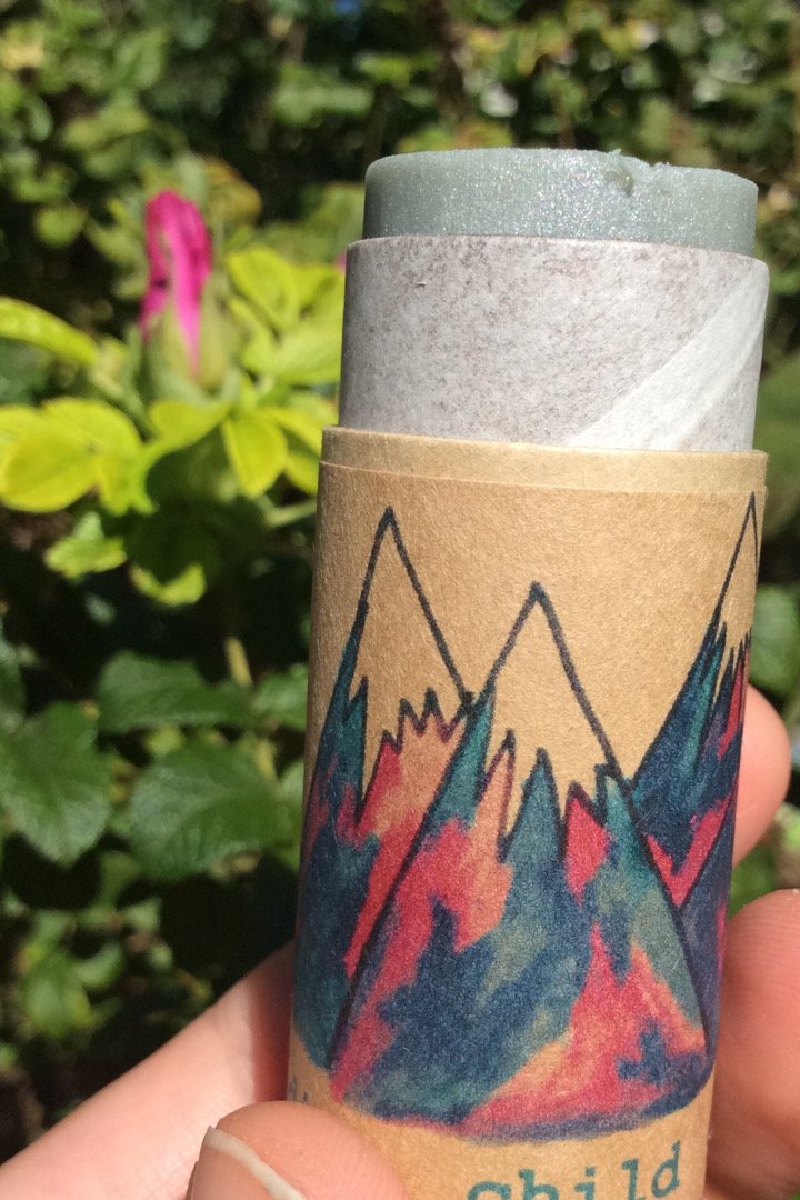 Cardboard tube of balm with colorful mountain design held against a natural background